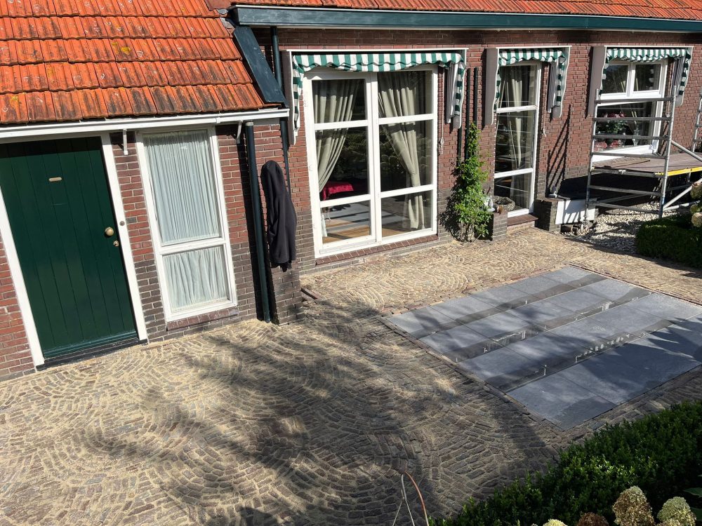 Bestrating: Aanbrengen terras van keramische tegels (in drainagemortel van Romfix, dus geen onkruid en losliggende tegels). Rondom oude gebakken waaltjes (breuksteen) verwerkt tot een prachtig geheel.